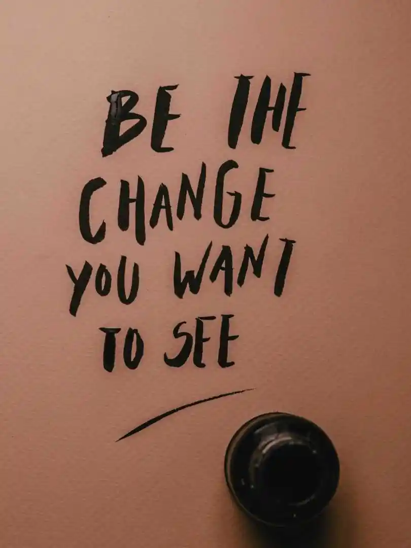 Inspirational message 'Be the change you want to see' in black ink on pink surface.