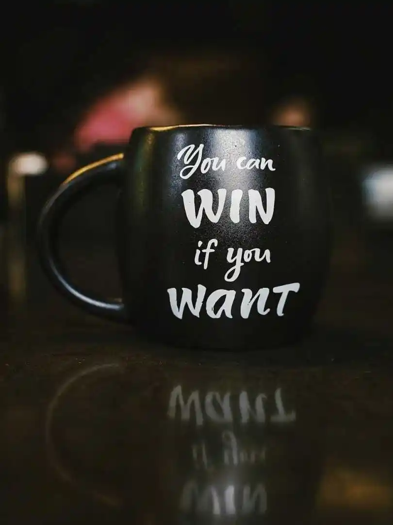 Black mug with inspirational quote 'You can win if you want' reflected on a dark surface, creating a motivational ambiance.